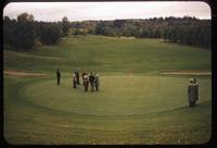 Group examining a mostly Poa annua green at the Mayfair golf course in Edmonton, 1955, with fairway beyond