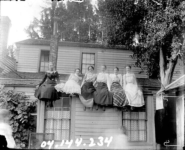 Six young women sitting on the roof of a house