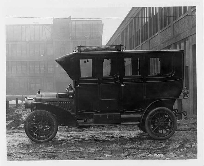 1908 Packard 30 Model UA by factory, two brick buildings in background