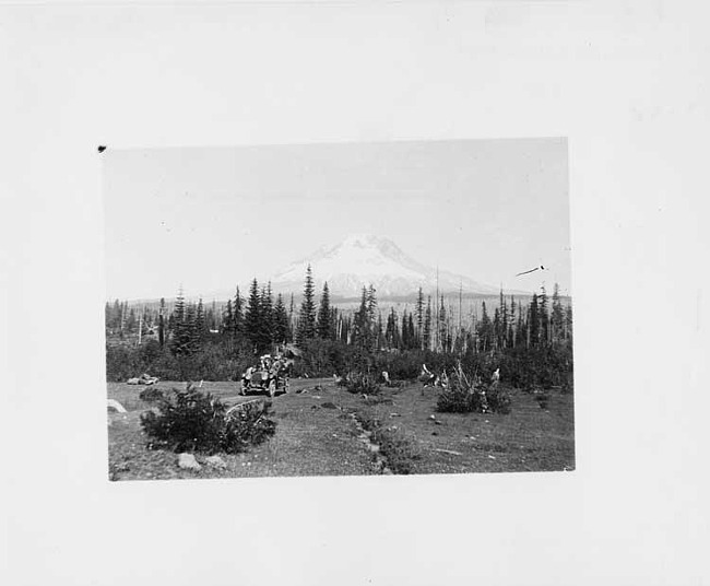 1910 Packard 30 Model UC, with passengers, pine trees and large snow covered mountain in background