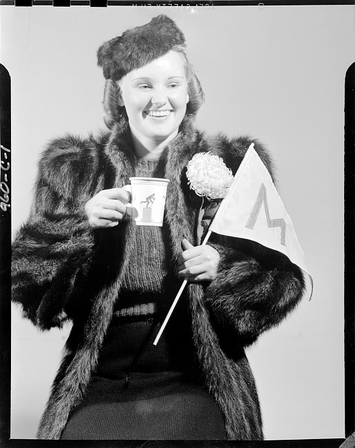Woman in fur coat holding flag and cup with hockey player figure