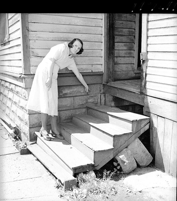 Woman on back porch steps, pointing to damage