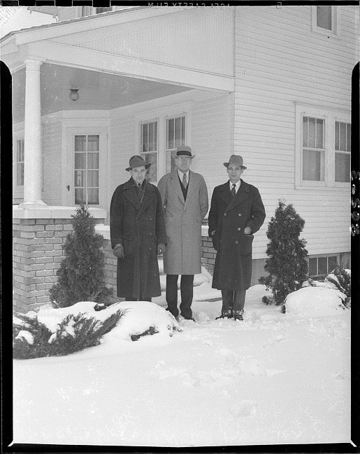 Three men in winter clothes posing in front of house