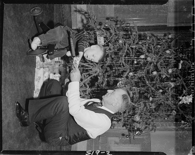 Boy on tricycle with elderly man by Christmas tree