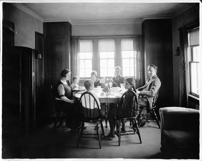 Family seated around dining room table, photograph