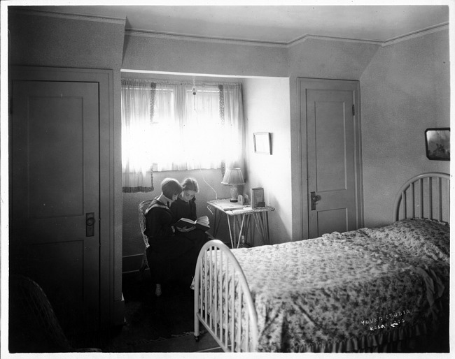 Two girls reading in bedroom, photograph
