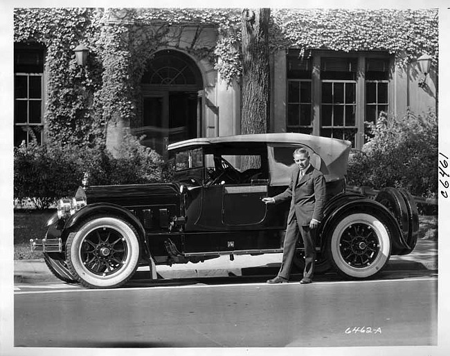 1916 Packard cloverleaf roadster parked on street in front of large, ivy-covered building