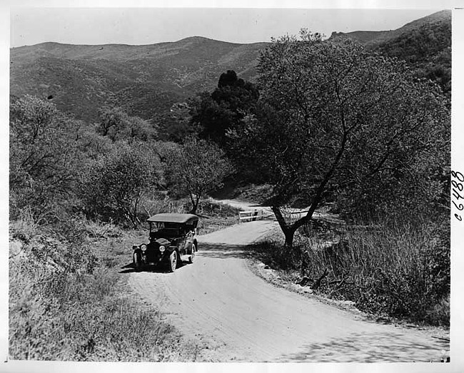 1917 Packard on country road with top raised and mountains in background