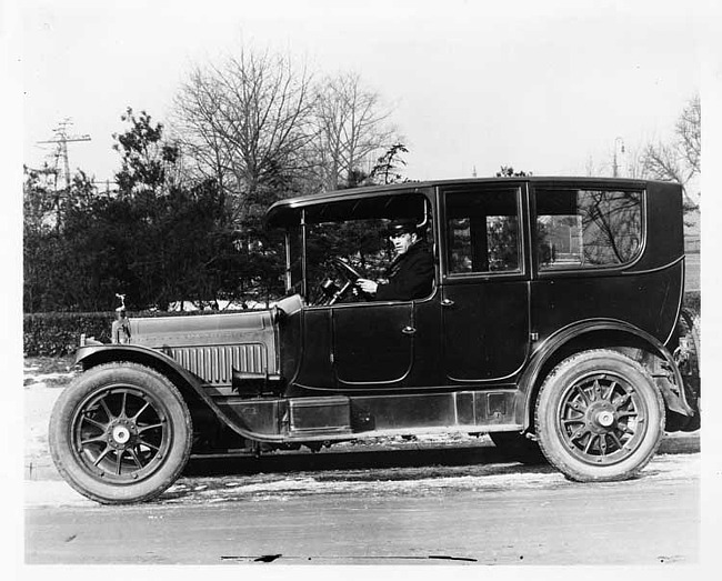 1917 Packard limousine with male chauffeur, parked on street, left side view