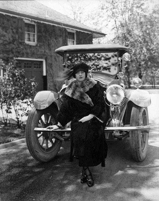 1922 Packard touring car, front view with female standing in front, parked on drive, garage in background