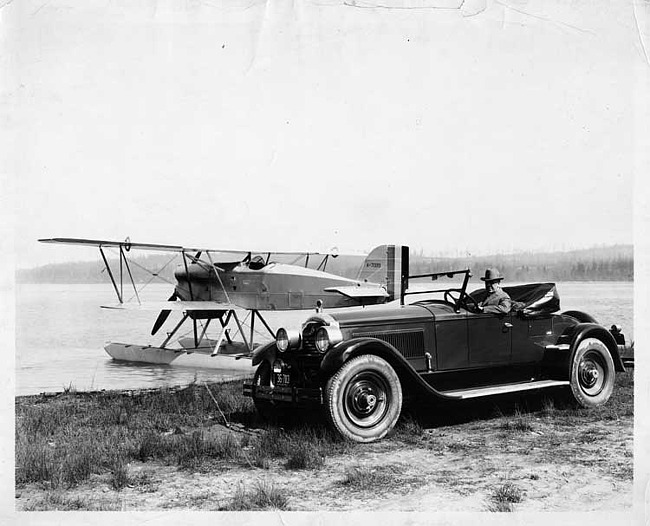 1924 Packard runabout parked next to lake with plane