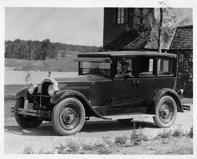 1925 Packard sedan, three-quarter left front view, male driver, parked in front of large home