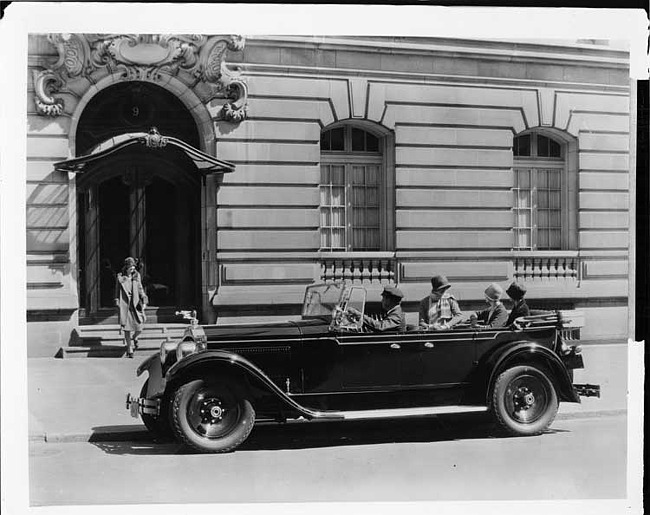 1928 Packard touring car parked on street with male chauffeur