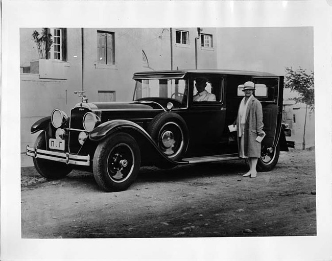 1929 Packard sedan limousine, male chauffeur, female standing at passenger door