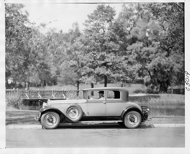 1930 Packard coupe, left side view, male driver, in a park like setting