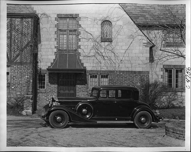 1933 Packard coupe, left side view, parked on driveway in front of large brick house