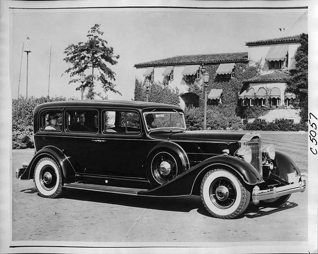 1934 Packard sedan, seven-eights right side view, couple seated in back, male driver