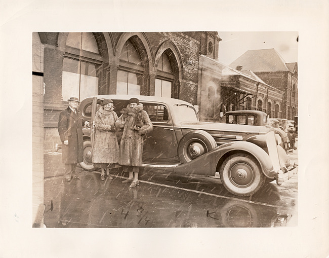 1936 Packard sedan, male holding rear passenger door open for two females