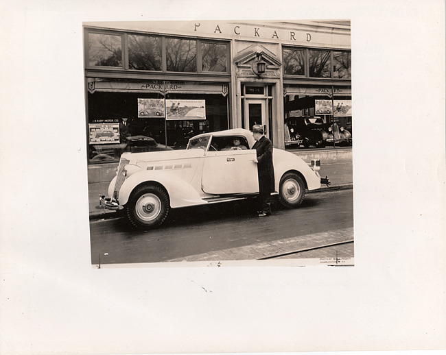 1936 Packard convertible coupe, top raised, in front of Packard dealership