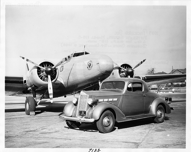 1937 Packard business coupe, parked on air strip in front of Boeing airplane