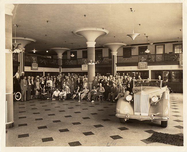 1937 Packard convertible sedan in showroom with crowd around it