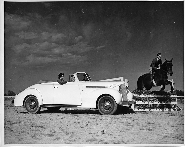 1939 Packard convertible coupe parked next to an equestrian jump fence