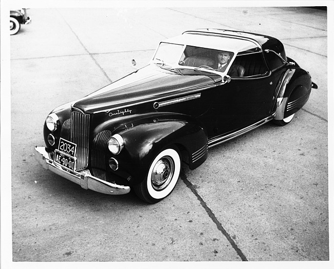 1941 Packard convertible victoria, three-quarter left front view, top raised, male behind wheel