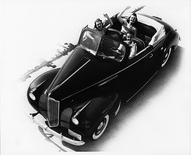 1941 Packard deluxe convertible coupe, top folded, male driver with two female passengers