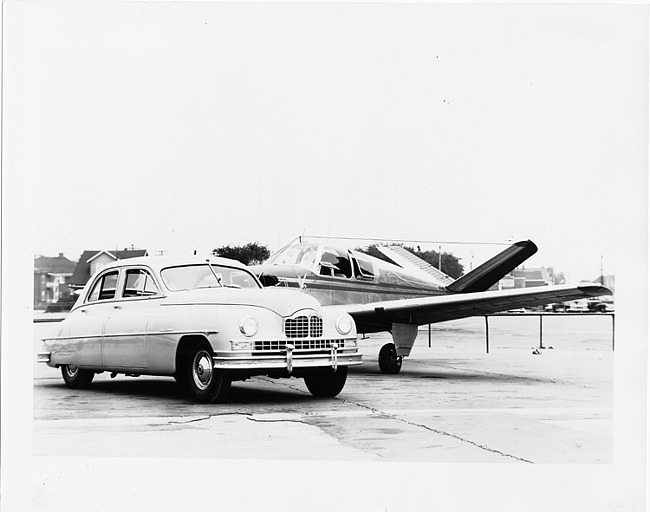 1949 Packard sedan parked on airstrip in front of single-engine airplane