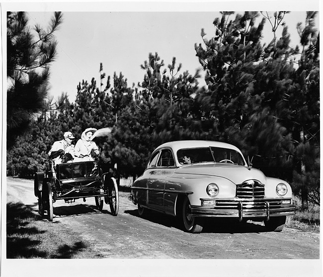 1949 Packard sedan, coming alongside 1899 Packard model A with two occupants