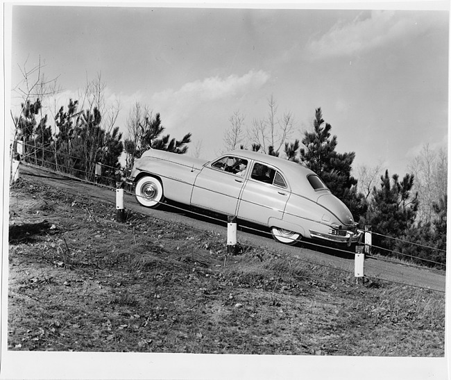 1949 Packard sedan, left side view, driving up steep hill, male behind wheel