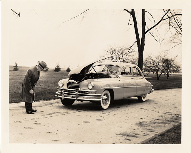 1950 Packard sedan, hood raised, man inspecting front of car