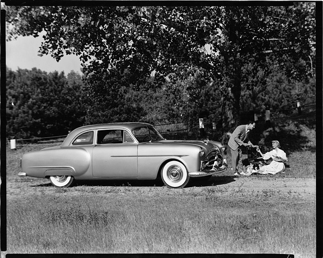 1951 Packard sedan, couple having a picnic under tree near front of car