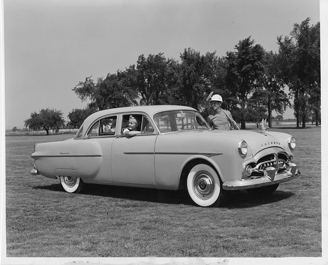1951 Packard 300 sedan parked on grass with man in polo uniform