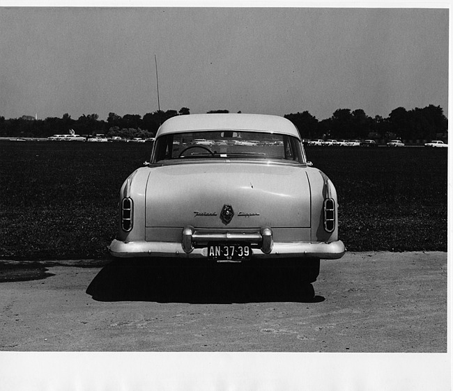 1953 Packard sedan, rear view, parked on drive, cars in distance