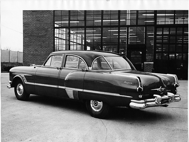 1953 Packard 4-door sedan, seven-eights rear left view, parked in drive near building