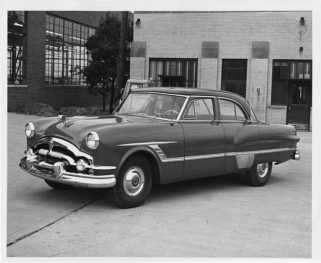 1953 Packard 4-door sedan, three-quarter left side view, parked in drive near brick building