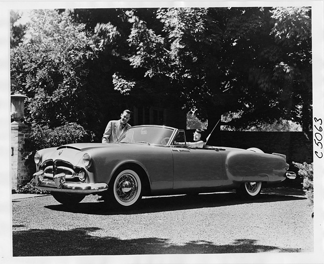 1953 Packard Pan American convertible, three-quarter left side view, parked in driveway, female behind wheel, man standing at passenger door