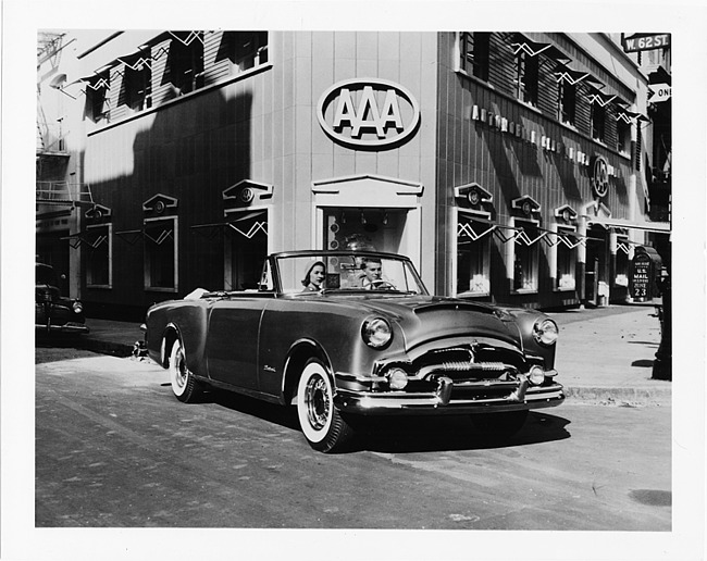 1953 Packard Caribbean convertible, top folded, parked on street in front of AAA building