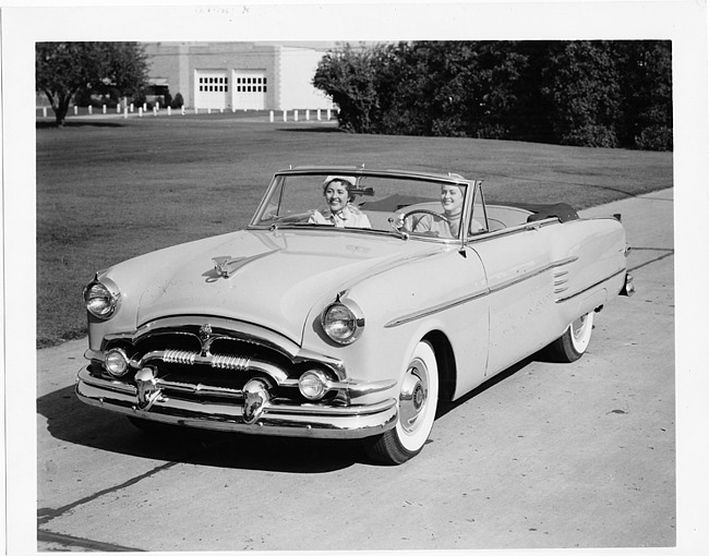 1954 Packard convertible, three-quarter front left view, top folded, two females in front seat