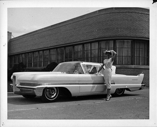 1956 Packard Predictor, female standing at driver's door, parked on street by brick building