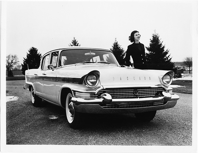 1957 Packard Clipper sedan, three-quarter front view, female standing at driver's door