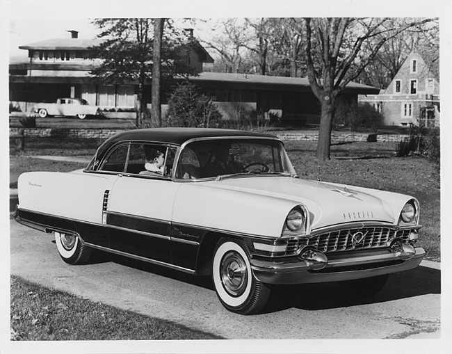 1955 Packard sedan parked in driveway, couple sitting in front seat