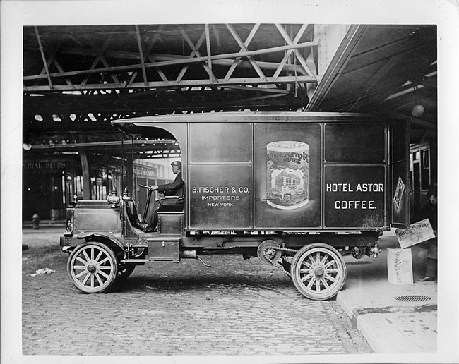 1911-12 Packard truck, left side view, man in driver seat, parked in loading area