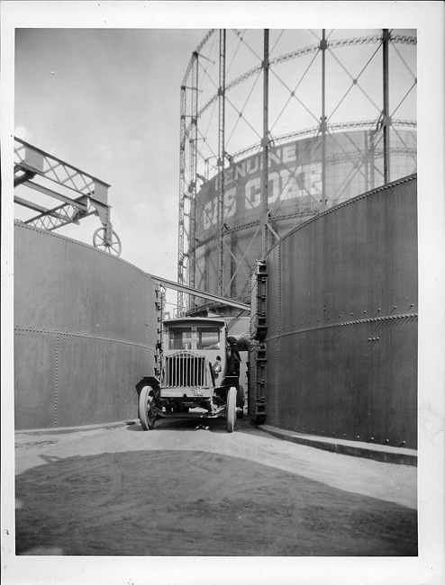 1922 Packard truck, front view, parked between two large metal cylinder tanks