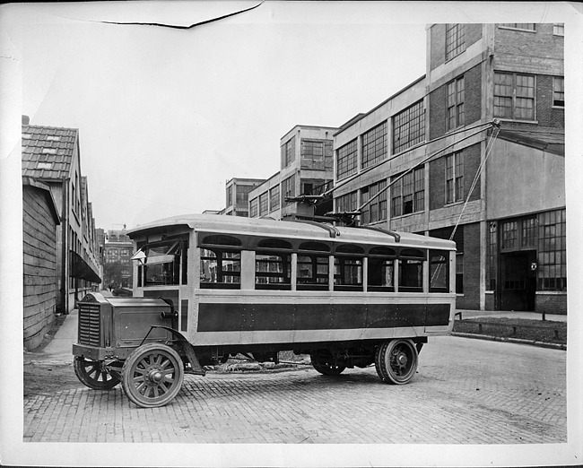 Packard electric bus, right side view, parked on brick-paved street