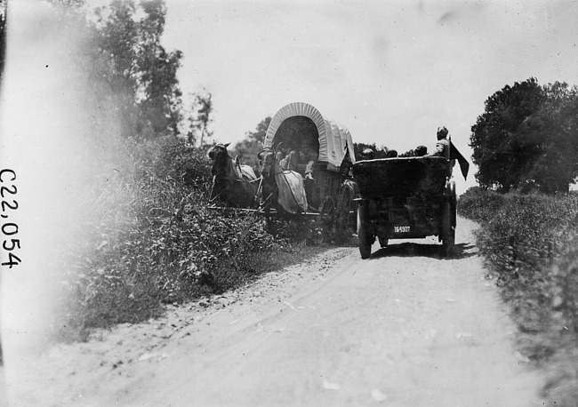 Participants passing covered-wagon in the 1909 Glidden Tour