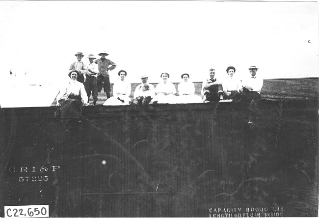 Group of people sitting on top of railroad car in Kearney, Neb., at 1909 Glidden Tour