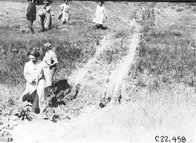 Woman walking through large hole in road near Aurora, Colo., at 1909 Glidden Tour