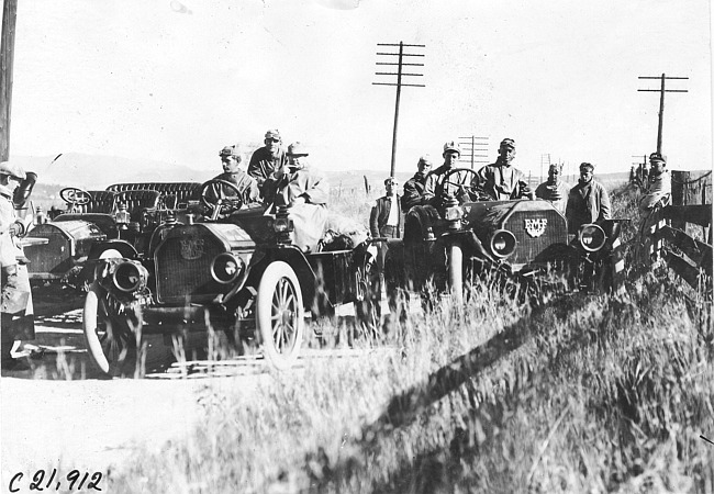 Glidden tourists pose near vehicles on rural road in Colo., at 1909 Glidden Tour